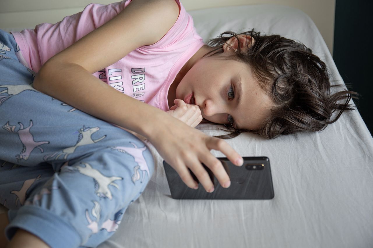 The girl is concentratedly playing a game on the smartphone while lying in bed in the morning. Smartphone addiction concept.